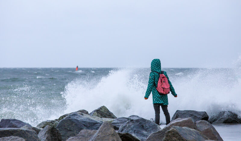Frau steht bei starkem Sturm an der Küste eines Meeres @ https://stock.adobe.com